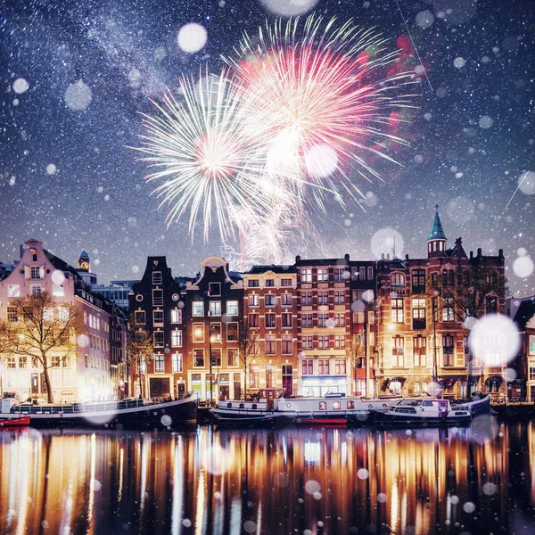 Beautiful night in Amsterdam. Night illumination of buildings and boats near the water in the canal. Photo greeting card. Colorful fireworks on the black sky background
