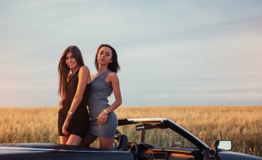 Yol kenarındaki yollarda siyah bir arabada iki kadın.