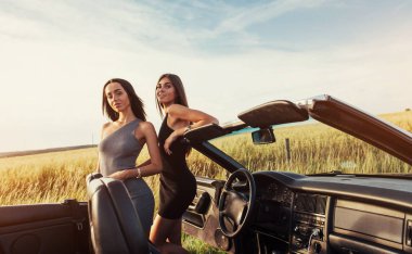 Bir lüks modern otomobil açık bir çatı ile seyahate zevk üstü açık bir arabayla oturan güzel iki kadın.