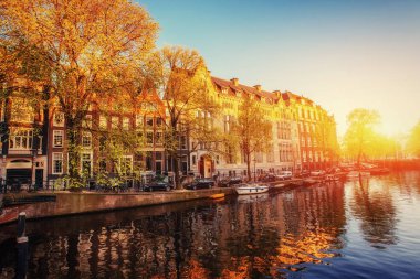 Binalar üzerinde parlar ve suya yansıyan fantastik günbatımı. Amsterdam Hollanda başkenti ve en kalabalık şehridir. 