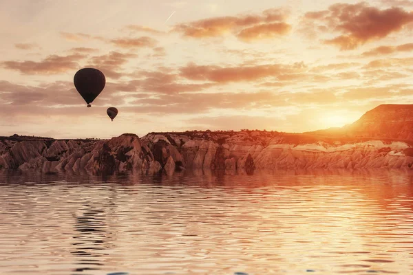 Composition of balloons over water and valleys, gorges, hills, between the volcanic mountains at sunset. Cappadocia, Turkey