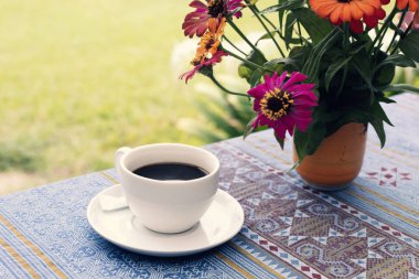 Siyah kahve ve çiçek vazo masada bir fincan.