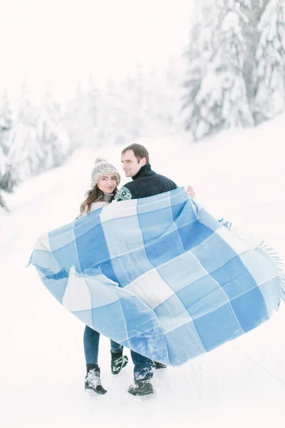 恋爱中的年轻夫妇在冬天的雪林里散步, 手里拿着温暖的羊毛毯子 — 图库照片
