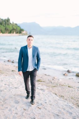 Garda Gölü kıyısında yürüyüş mavi ceketli genç yakışıklı esmer adam. İtalya.