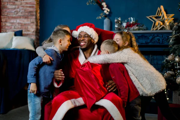 Niños Abrazando Papá Noel Africano Sentado Una Silla Roja Fondo — Foto de Stock