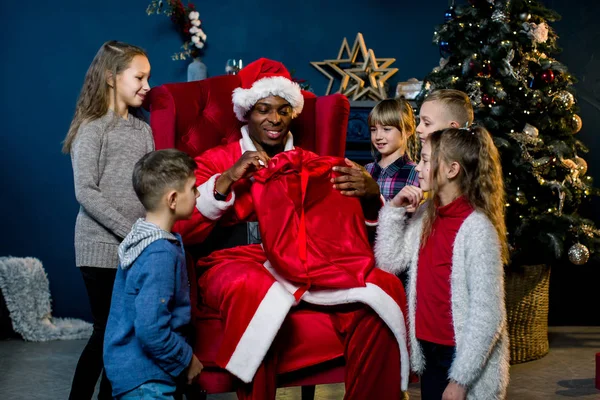 アフリカのサンタ クロースがクリスマス ツリーの背景の上に座っているし 子供たちに贈り物をプレゼント — ストック写真