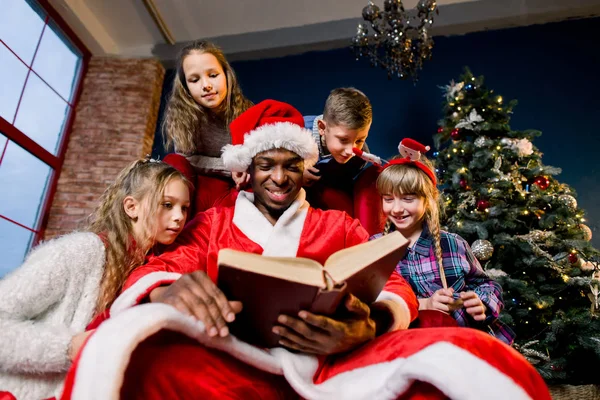 サンタ クロースは クリスマス装飾の部屋で小さく 美しい子供のため大まかな古書を読み取ります — ストック写真