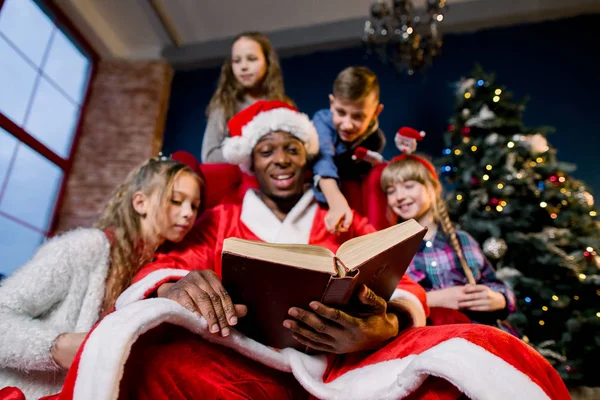 サンタ クロースは クリスマス装飾の部屋で小さく 美しい子供のため大まかな古書を読み取ります — ストック写真