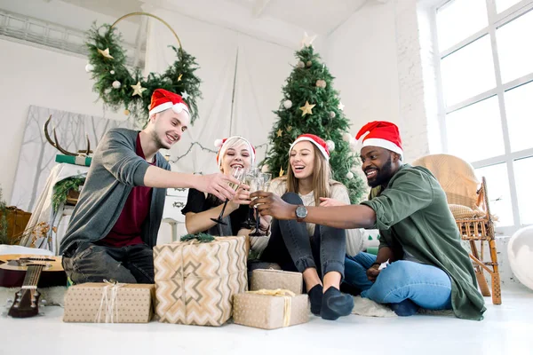 アフリカ青年と白人男性と女性 サンタの帽子とクリスマス クリスマスと新年の祝賀パーティーのシャンパンを飲むグラスをチャリンという音します — ストック写真