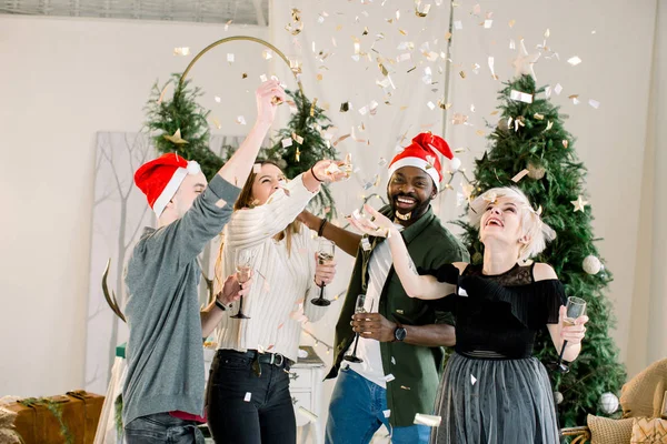 陽気なファッションのグループを着て友人のクリスマスの装飾の前に立ってとシャンパンを飲み 新しい年を祝う — ストック写真