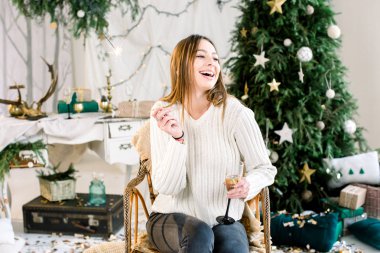 Neşeli Genç beyaz bir kadın, beyaz kazak gülüyor ve holding Bengal ışık ve cam şampanya ile ördü. Neşeli Noel, yeni yıl, Aile, tatil kavramı.
