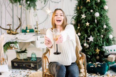 Neşeli Genç beyaz bir kadın, beyaz kazak gülüyor ve holding Bengal ışık ve cam şampanya ile ördü. Neşeli Noel, yeni yıl, Aile, tatil kavramı.