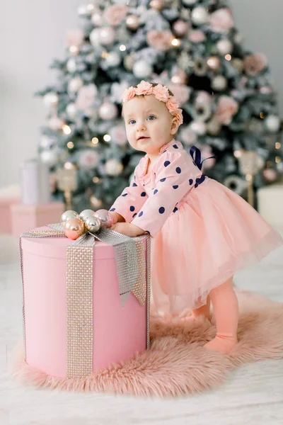 クリスマス ツリーや装飾品の背景に美しいクリスマス ボックスの近くでピンクのドレスかわいい赤ちゃん クリスマス 新しい年のコンセプト — ストック写真