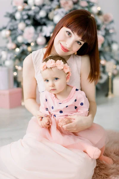クリスマスと幸せな新年の休日 母と子のコンセプトです 幸せママと楽しく 室内のクリスマス ツリーのそばに一緒に座ってピンクのドレスを着て彼女のかわいい女の子 — ストック写真