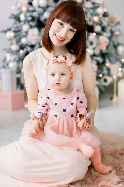 クリスマスと幸せな新年の休日 母と子のコンセプトです 幸せママと楽しく 室内のクリスマス ツリーのそばに一緒に座ってピンクのドレスを着て彼女のかわいい女の子 — ストック写真