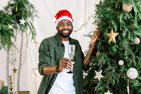 크리스마스 트리 근처 샴페인을 들고 매력적인 미소로 아프리카 미국 사람 — 스톡 사진