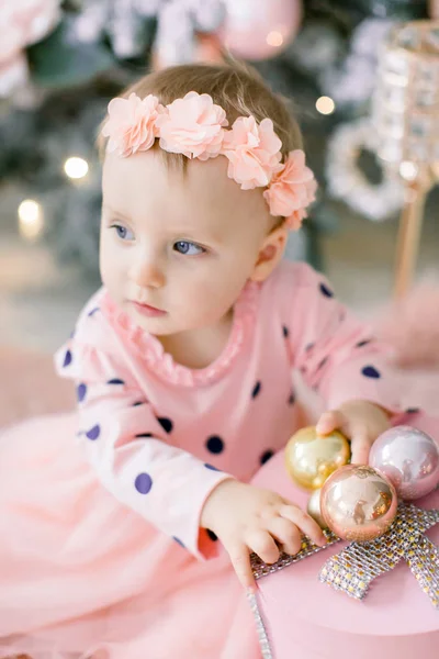 Menina feliz bonito em luz vestido laranja brinca com presentes de Natal e senta-se no tapete peludo rosa perto de uma árvore de Natal. Família, Natal, Conceito de Ano Novo . — Fotografia de Stock