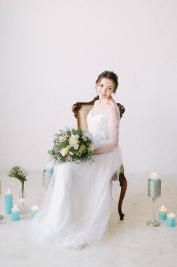 Beyaz elbiseli güzel gelin romantik bir şekilde dekore edilmiş oda dekore edilmiş mumlar ve çiçeklerle vintage sandalyede oturuyor. Studio fotoğraf