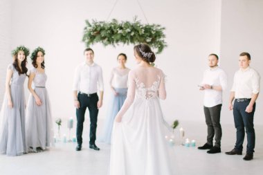 Beyaz elbiseli güzel gelin düğün buket tutar ve onun damat nedime ve groommen düğün töreni için gidiyor. Beyaz Oda çam, çiçek ve mavi mum ile süslüdür.