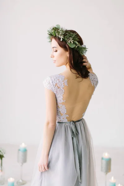 灰色のイブニング ドレスと松と結婚式風景の背景に彼女の頭のポーズにユーカリのリースの美しい少女 結婚式前にスタジオの Bridesmade ポーズ — ストック写真