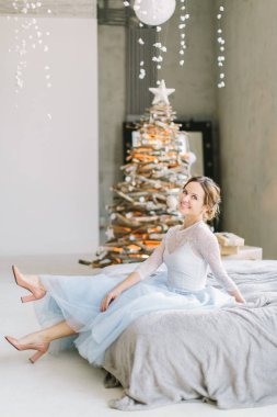 Yatakta Noel ağacı arka plan üzerinde oturan mavi beyaz elbiseli Genç ve güzel kadın
