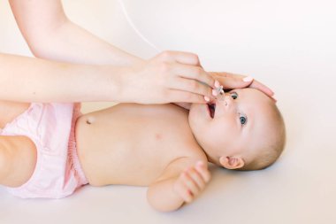 Mother using baby nasal aspirator. She is doing a mucus suction to four months baby girl clipart