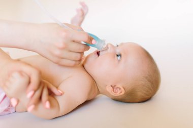 Elleri küçük bir kız için başını tutan anne bebek burun Aspiratörü aracılığıyla yatakta yalan sümük berbat. Yatakta burun Temizleme.