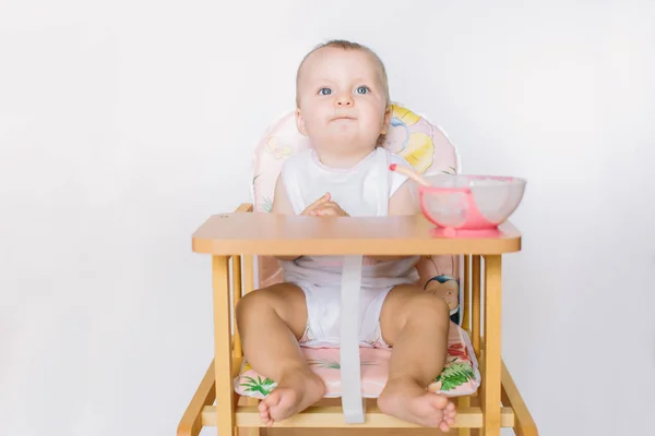 The baby is sitting on the chair and is preparing for feeding.