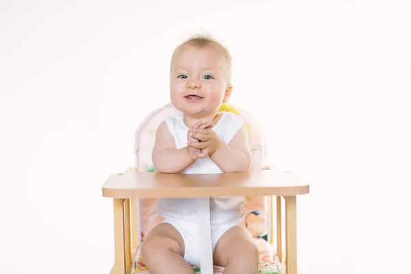 The baby is sitting on the chair and is preparing for feeding.