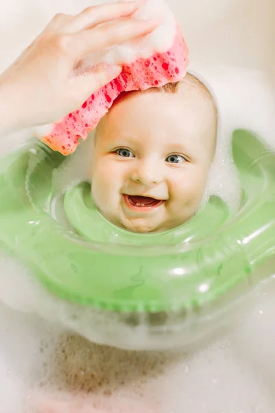 婴儿游泳与绿色的脖子游泳环 妈妈用红色海绵清洗婴儿头 — 图库照片