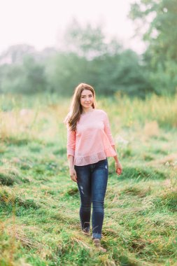Güzellik genç kız açık havada doğanın keyfini. Pembe tişört ve kot çayırda genç kadın moda