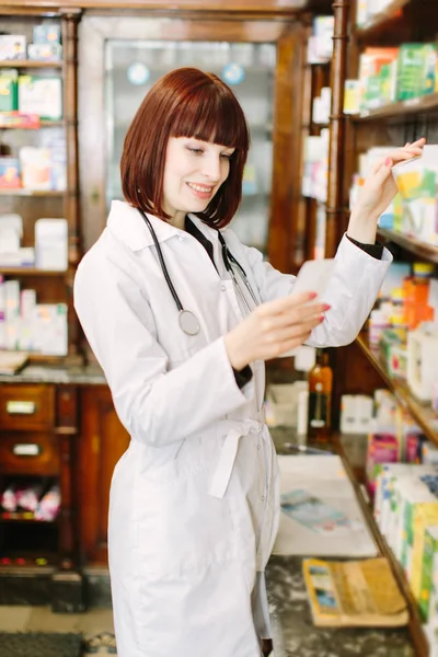 Pretty young pharmacist reading the information about medicine and choosing the product in pharmacy