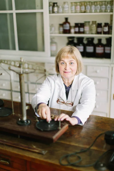 Smiling attractive middle-aged blond lady pharmacist working with vintage scales in the pharmacy