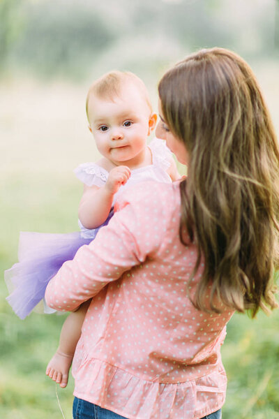 Young mother holding daughter in her arms. Beautiful Mother And Baby outdoors. Nature. Beauty Mum and her Child playing in Park together. Outdoor Portrait of happy family. Joy. Mom and Baby