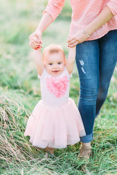 緑の草 サポート歩くことを学ぶことで彼女の手を繋いで母親に彼の最初のステップを作るかわいい面白いハッピー ベビー女の子 — ストック写真