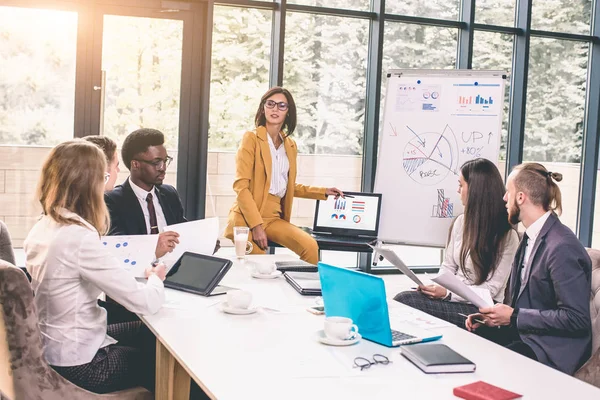 Businesswoman Stands To Address Meeting Around Board Table