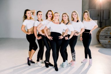Beyaz ve siyah kıyafeti ayakta beyaz duvar adlı genç sportif kız grubudur. Fitness, kapalı tam uzunlukta, çatı sonra stüdyo, spor salonu dinlenme içinde kadın arkadaşlık alanı kopyalayın