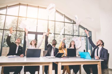 iş adamları mutlu bir gülümseme, atmak kağıtları heyecanlı, belgeleri havada uçmak, ofis masa başında oturan işadamı ellerini kollarını kaldır, başarı takım kavramı işaret sözleşme sonra tutun.