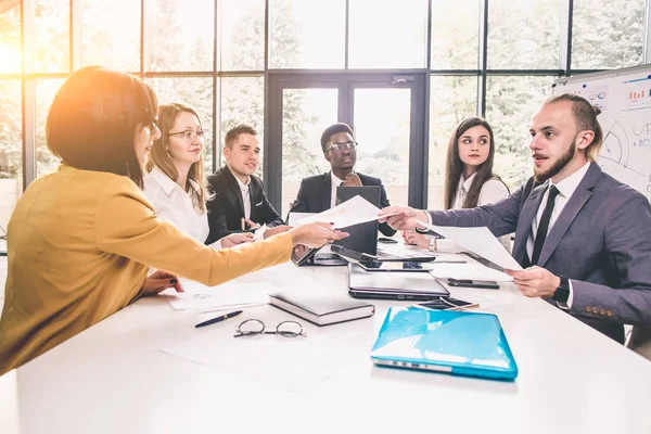 Portrait of a smiling group of diverse corporate colleagues sitting together at a table in a bright modern office. Business people sharing their ideas.