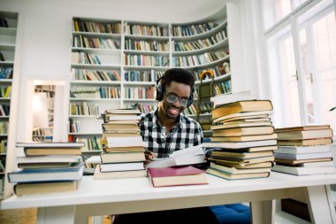 Sınavı için kitap okuma ve kütüphane Üniversitesi, eğitim ve okuma kavramı kulaklık ile müzik dinlemek öğrenci genç adam