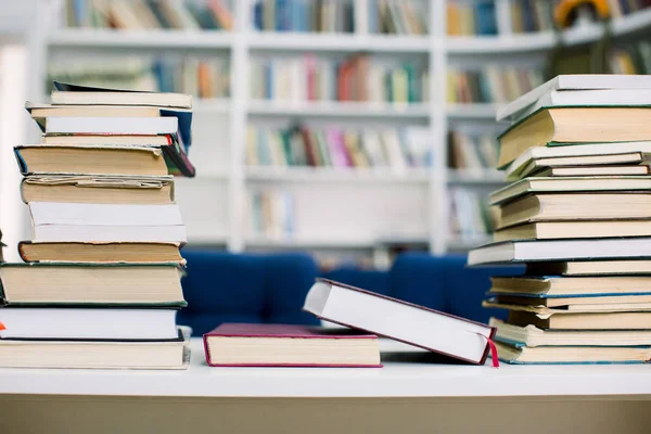 Stacks of paperback books, closeup, with the full bookshelf in the background. Searching for the right book in a bookstore. Piles of bestsellers.