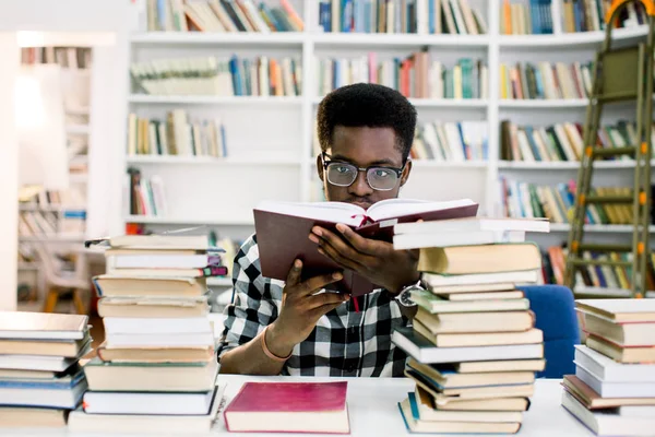 Konsantre siyah Avrupa erkek öğrenci araştırma üniversite Kitaplığı'nda çalışan sırt çantası ile samimi bir kadeh. Yurtdışında tatil önce kitapçı ifade kitapta arayan şık koyu tenli adam