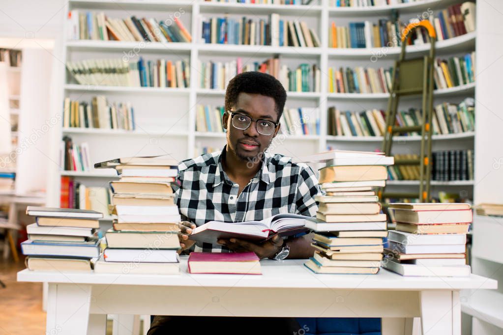 Candid shot of concentrated black European male student with backpack working on research in college library. Stylish dark-skinned man looking for phrase book in bookshop before vacations abroad