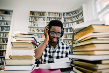 Kulaklıklar ile kütüphanede oturmuş ve bilimsel bir kitap okuma Afro-Amerikan öğrenci
