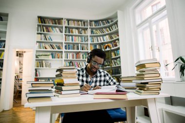 Güzel, esmer öğrenci öğrenci kulaklık ile bilimsel literatür, kalemle notlar yapma okur