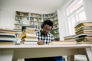 Güzel, esmer öğrenci öğrenci kulaklık ile bilimsel literatür, kalemle notlar yapma okur