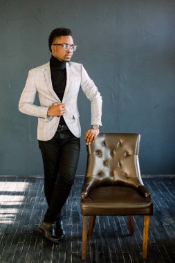 Esmer çekici yakışıklı mutlu gülümseyen yetişkin hakkında düşünme onun iş ayakta yakınındaki koyu arka plan üzerinde deri sandalye