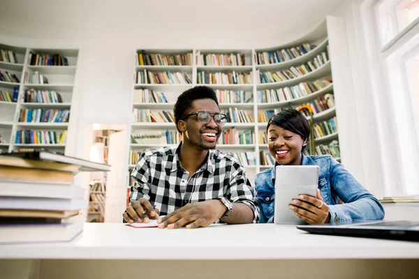 Young college african american students at the library studying together, they are smiling and leaning on a pile of books