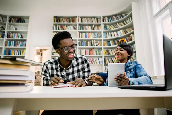 Young college african american students at the library studying together, they are smiling and leaning on a pile of books