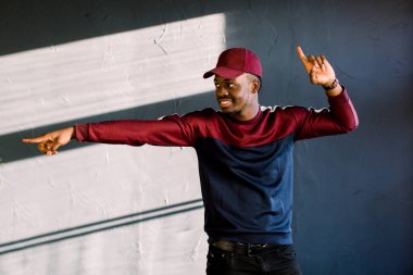 Komik adam koyu tenli hareketlerle mutlu bir şekilde gladfully onun başarısı, gülümsüyor gurur hissediyorum, koyu arka plan üzerinde izole eski moda kırmızı bere takıyor. İnsanlar, mutluluk ve sevinç kavramı